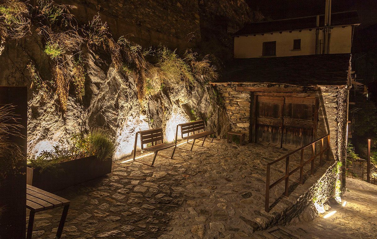 Una pasarela de piedra con bancos y una valla por la noche. Emfasi Estudi
