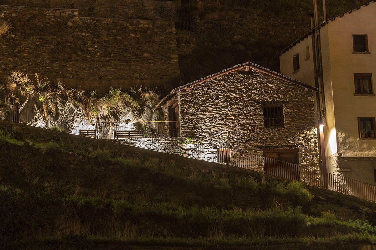 Un pequeño edificio de piedra se ilumina por la noche. Emfasi Estudi