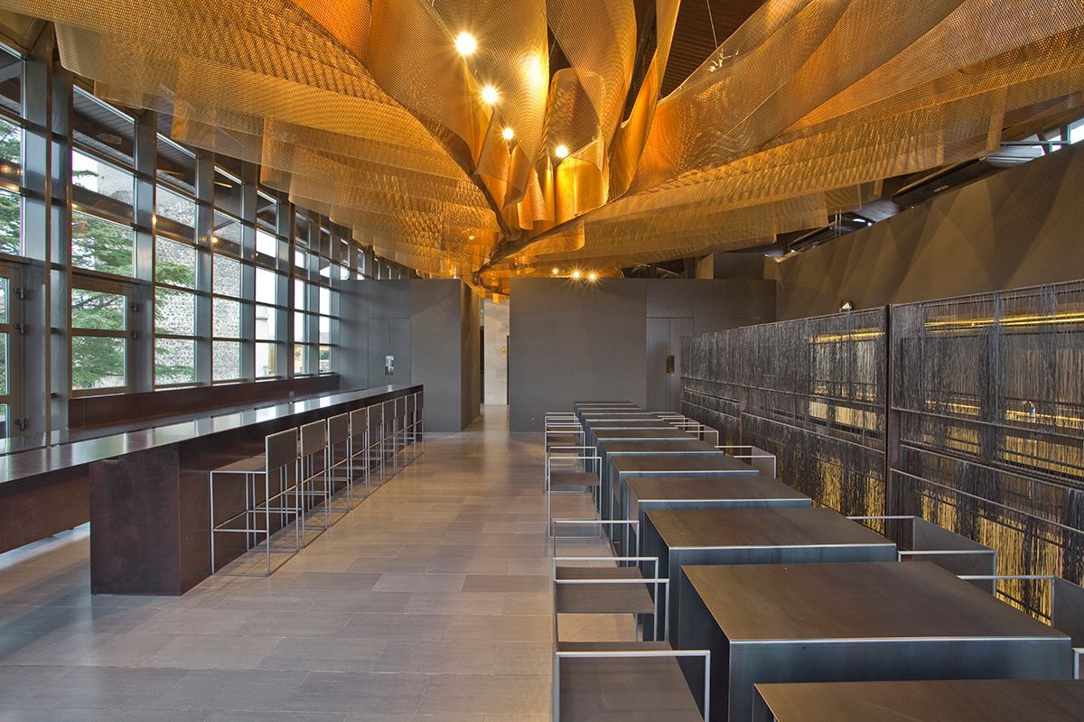 Fotografia Emfasi Estudi Andorra. Una sala larga con mesas y sillas y un techo que parece un árbol.