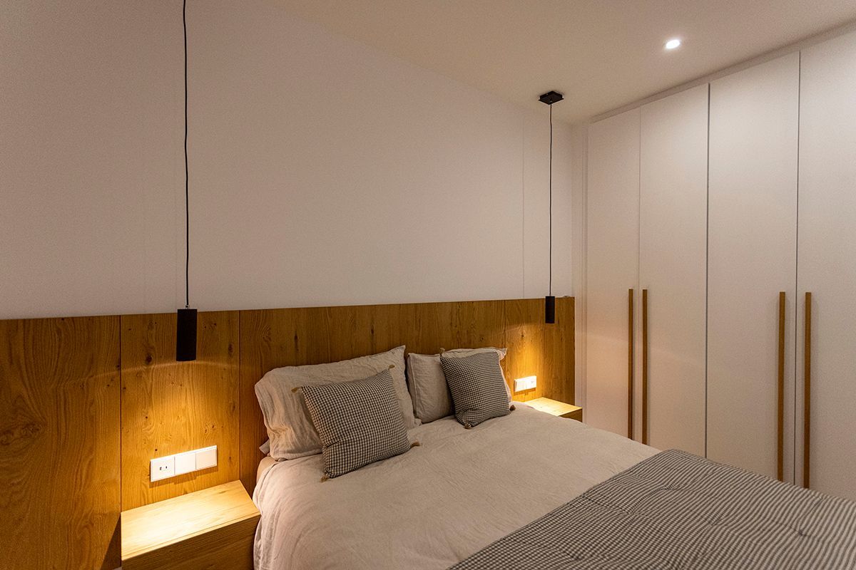En medio de la habitación hay una cama con cabecero de madera. Fotografia Emfasi Estudi Andorra.