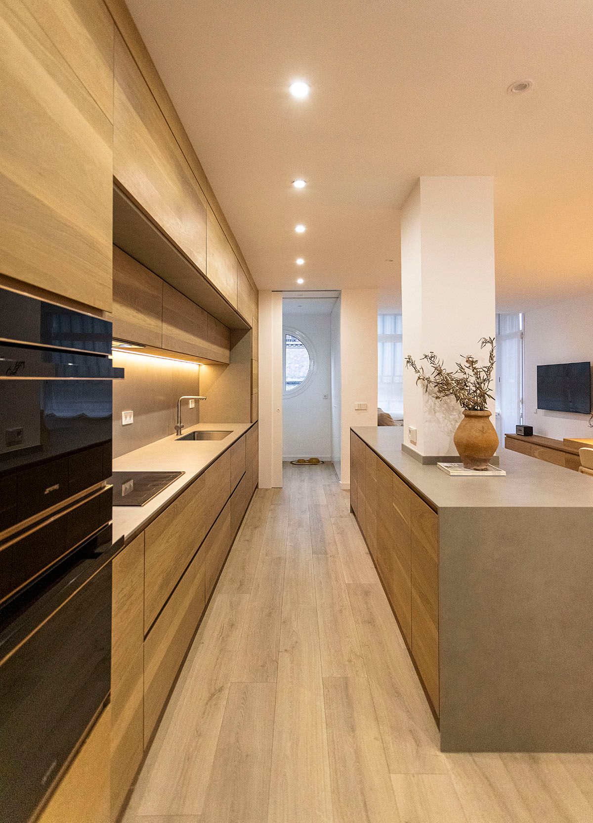 Una cocina larga con gabinetes de madera y una encimera gris. Fotografia de arquitectura. Fotografia Emfasi Estudi Andorra.