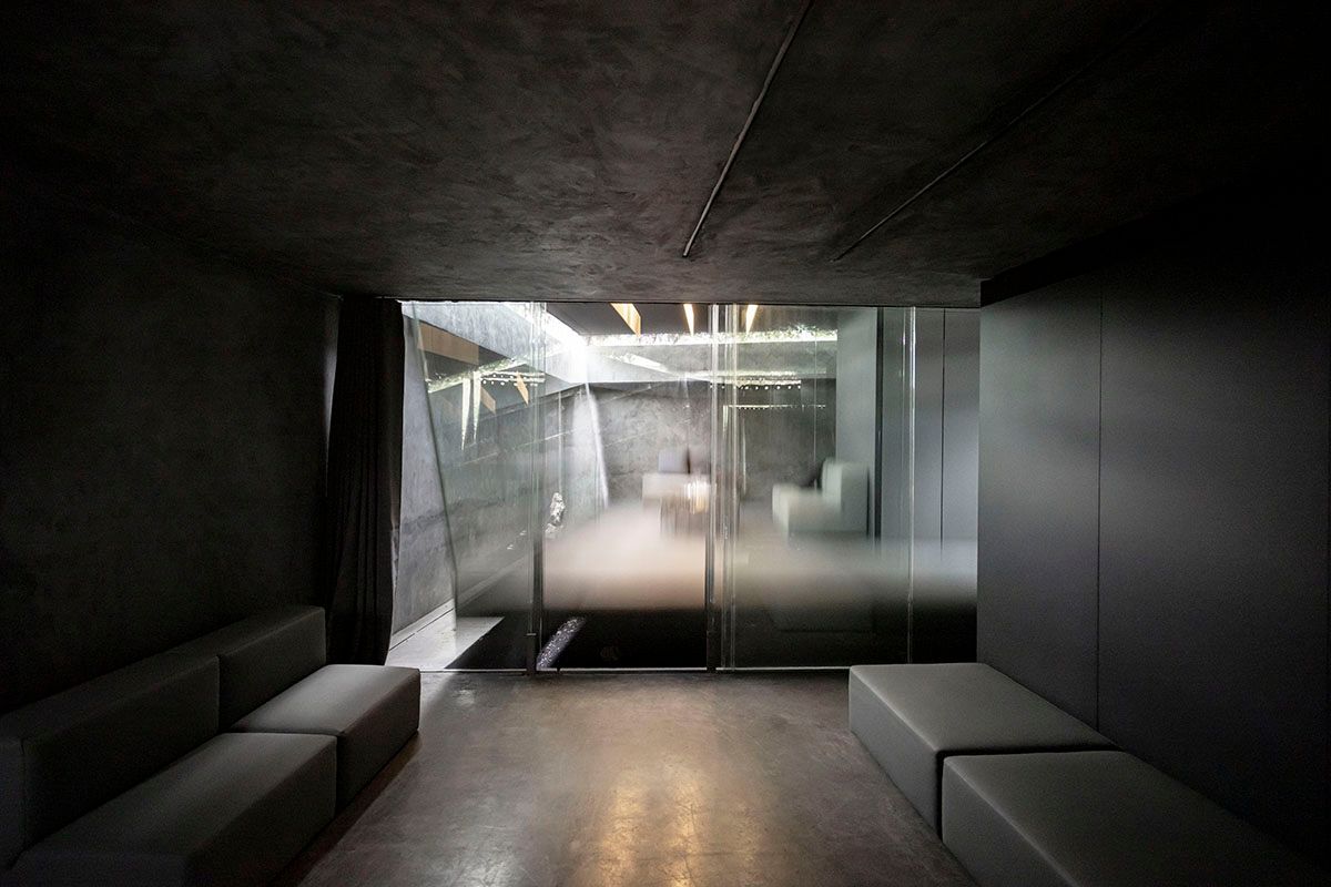 Fotografia Emfasi Estudi Andorra. Una habitación oscura con un sofá y una puerta de cristal. Arquitectura moderna.