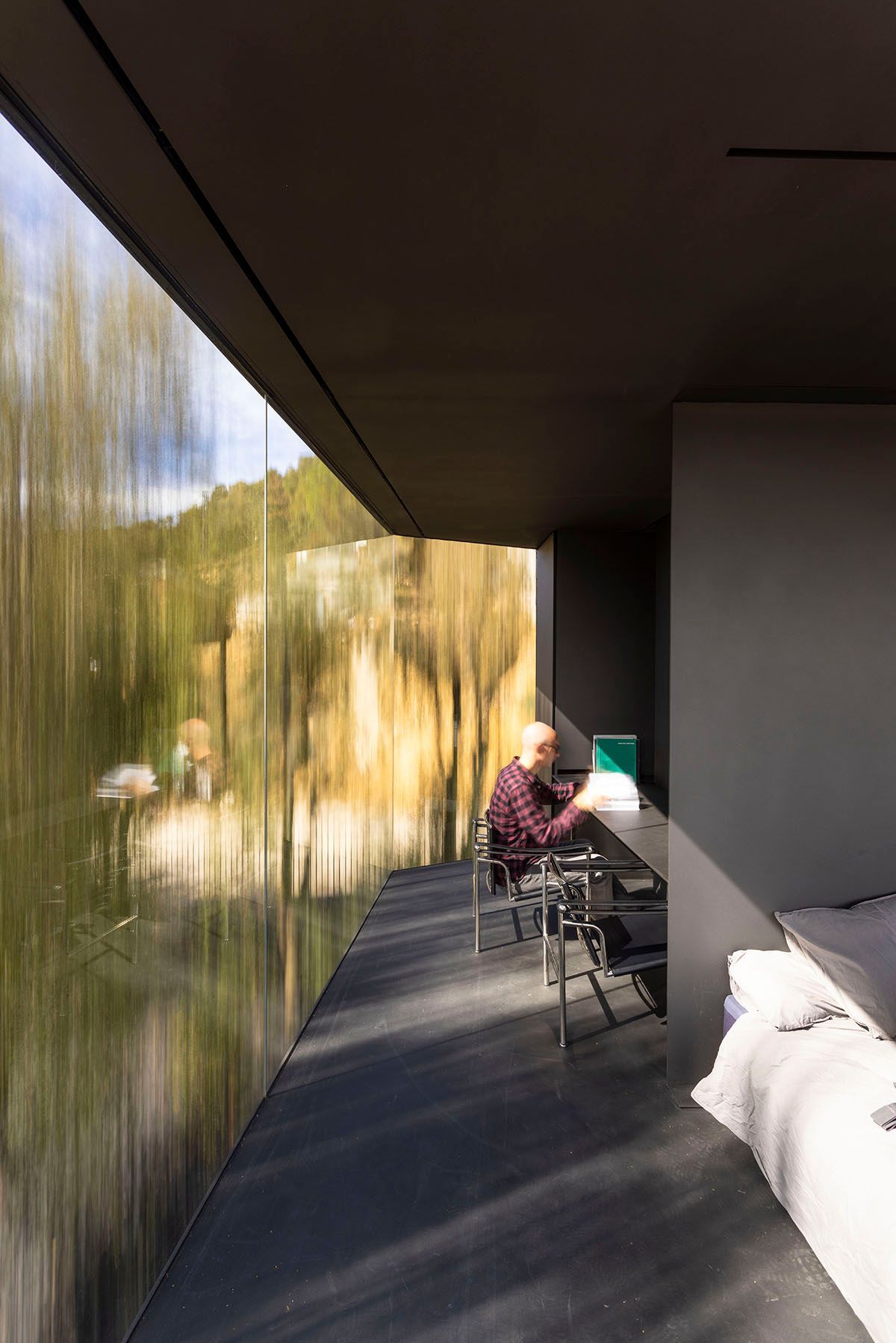 Fotografia Emfasi Estudi Andorra. Un hombre está sentado en un escritorio en una habitación con una ventana grande.