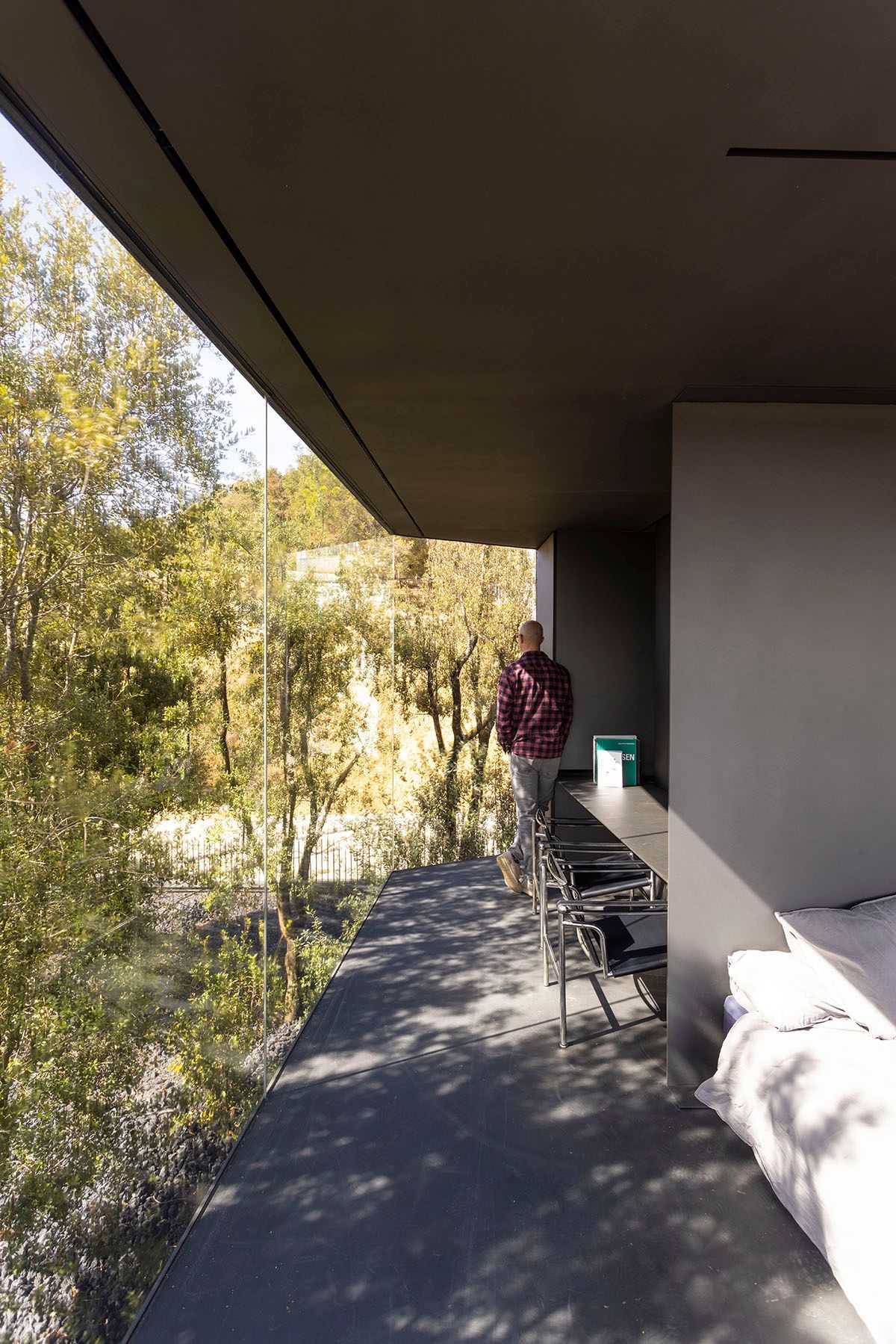 Fotografia Emfasi Estudi Andorra. Un hombre está parado en un balcón con vistas a un bosque. Casa moderna y espaciosa. 