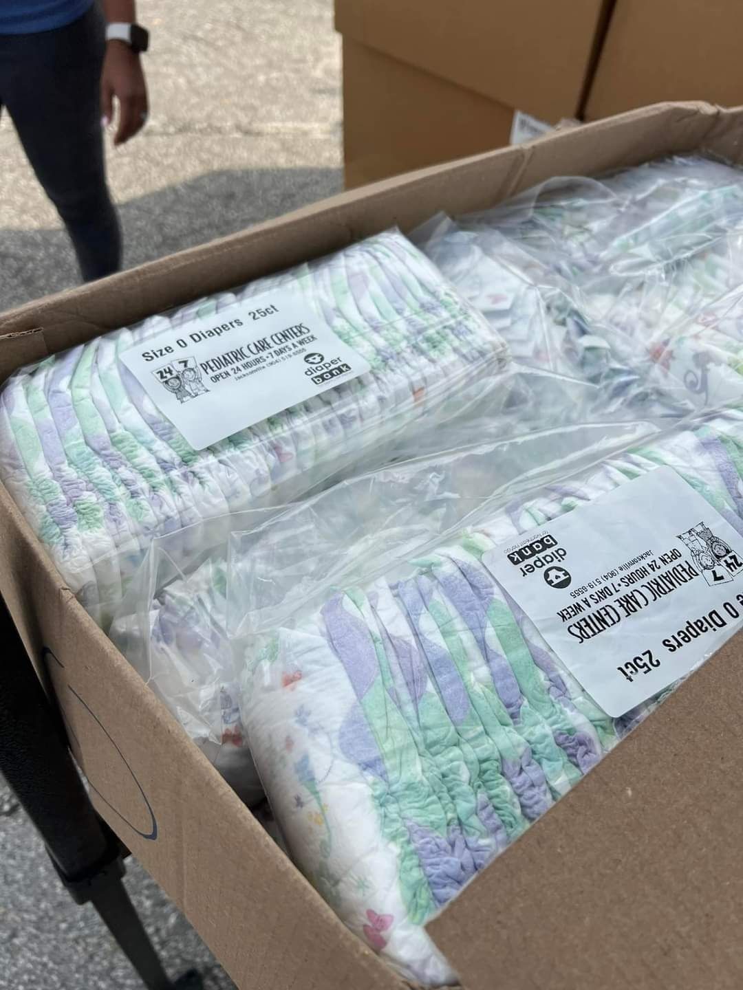 Box of sealed plastic-wrapped medical supplies with labels, outdoors on the ground