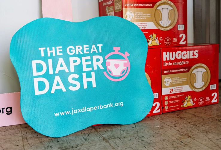 Blue sign reading “The Great Diaper Dash” beside stacked Huggies diaper boxes on a floor