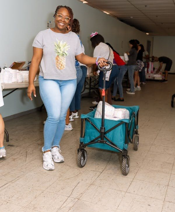 Woman standing beside a teal wagon in a hallway, smiling and holding its handle.