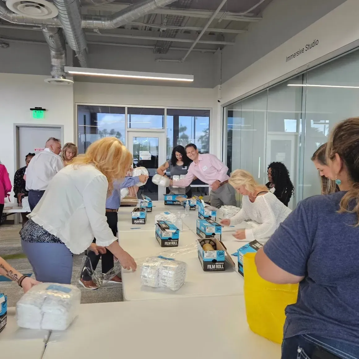 People packing snack bags around a long table in a bright office workspace