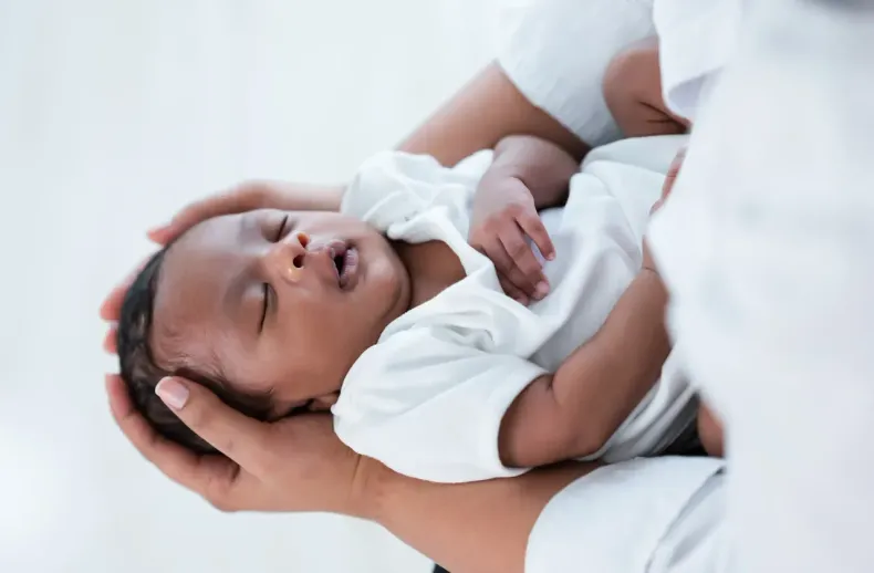 Sleeping baby held in an adult’s arms, with hands gently supporting the head