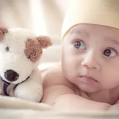 Baby lying next to a white teddy bear, gazing upward on a soft blanket.