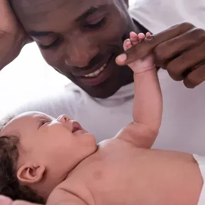 Parent gently holding a baby’s hand, both smiling and looking at each other