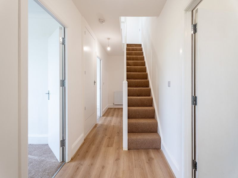 Hallway with stairs, light wood floors, white walls, and brown carpeted stairs.