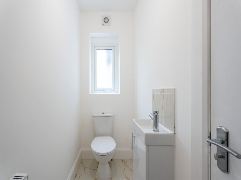 Small, white bathroom with toilet, sink, and window. Marble-look flooring and neutral walls.