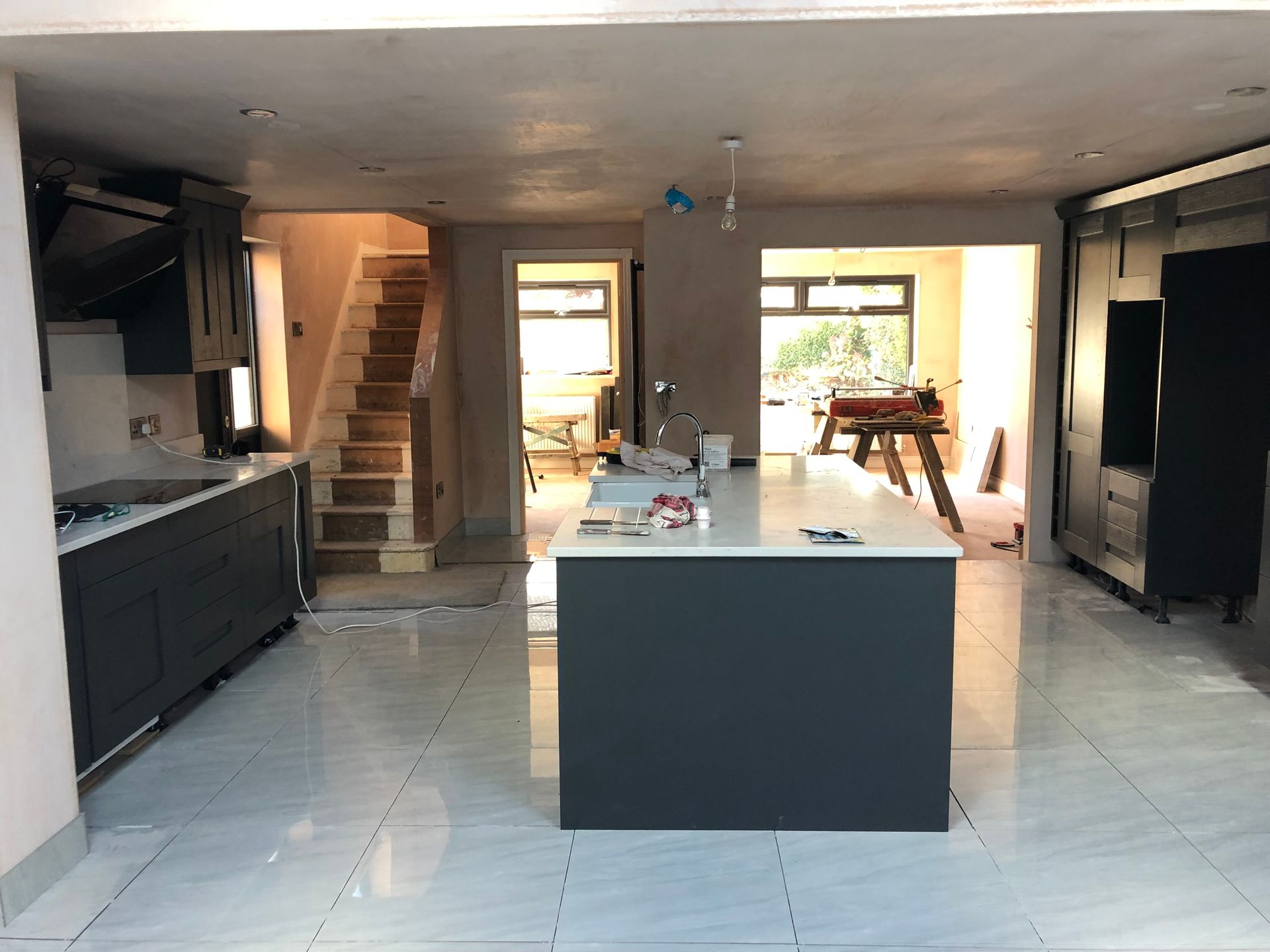 Modern kitchen under renovation, featuring gray cabinets, white countertops, tile flooring, and a central island.