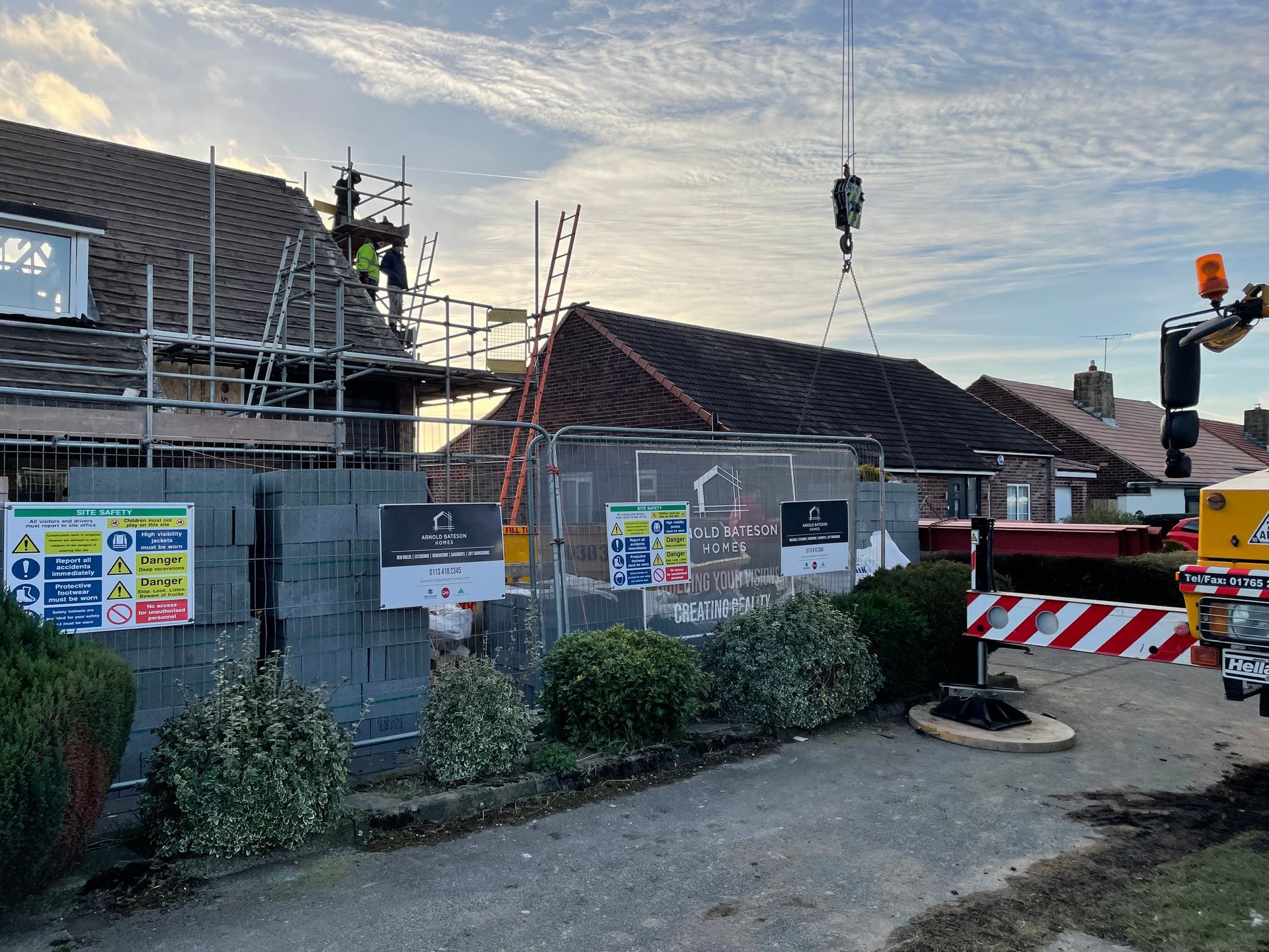 Construction site with scaffolding and a crane lifting materials, residential area.
