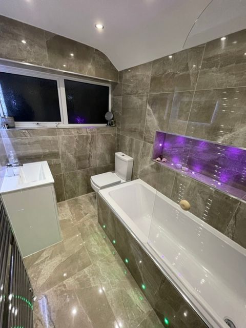 Modern bathroom with marble-look tiles, white fixtures, and purple LED lighting above the bathtub.