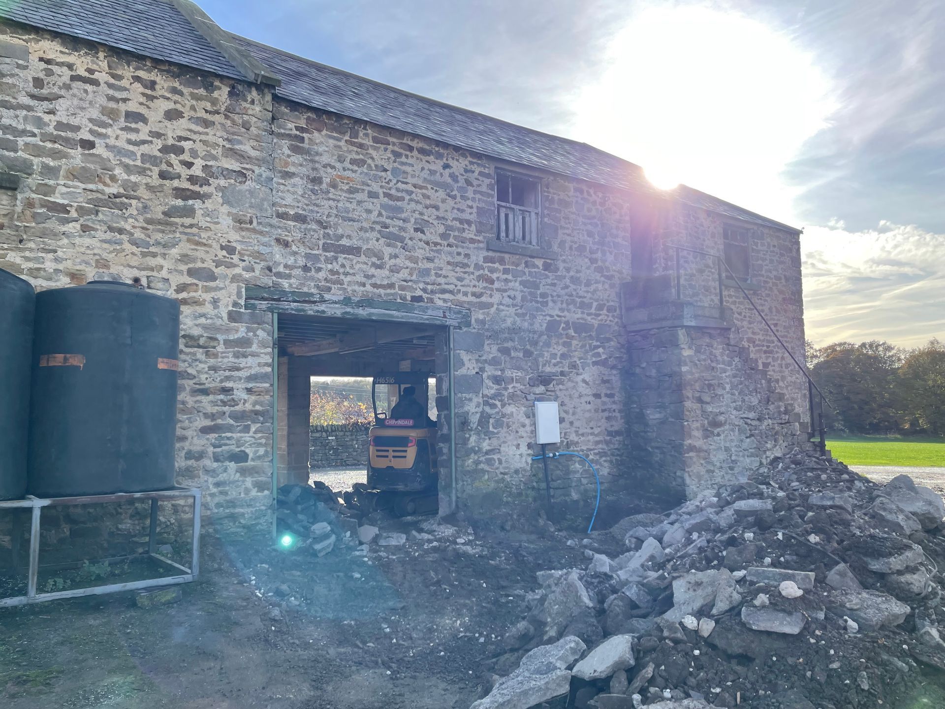 Stone barn with open doorway; a small tractor is inside. Sunlight shines on the building.