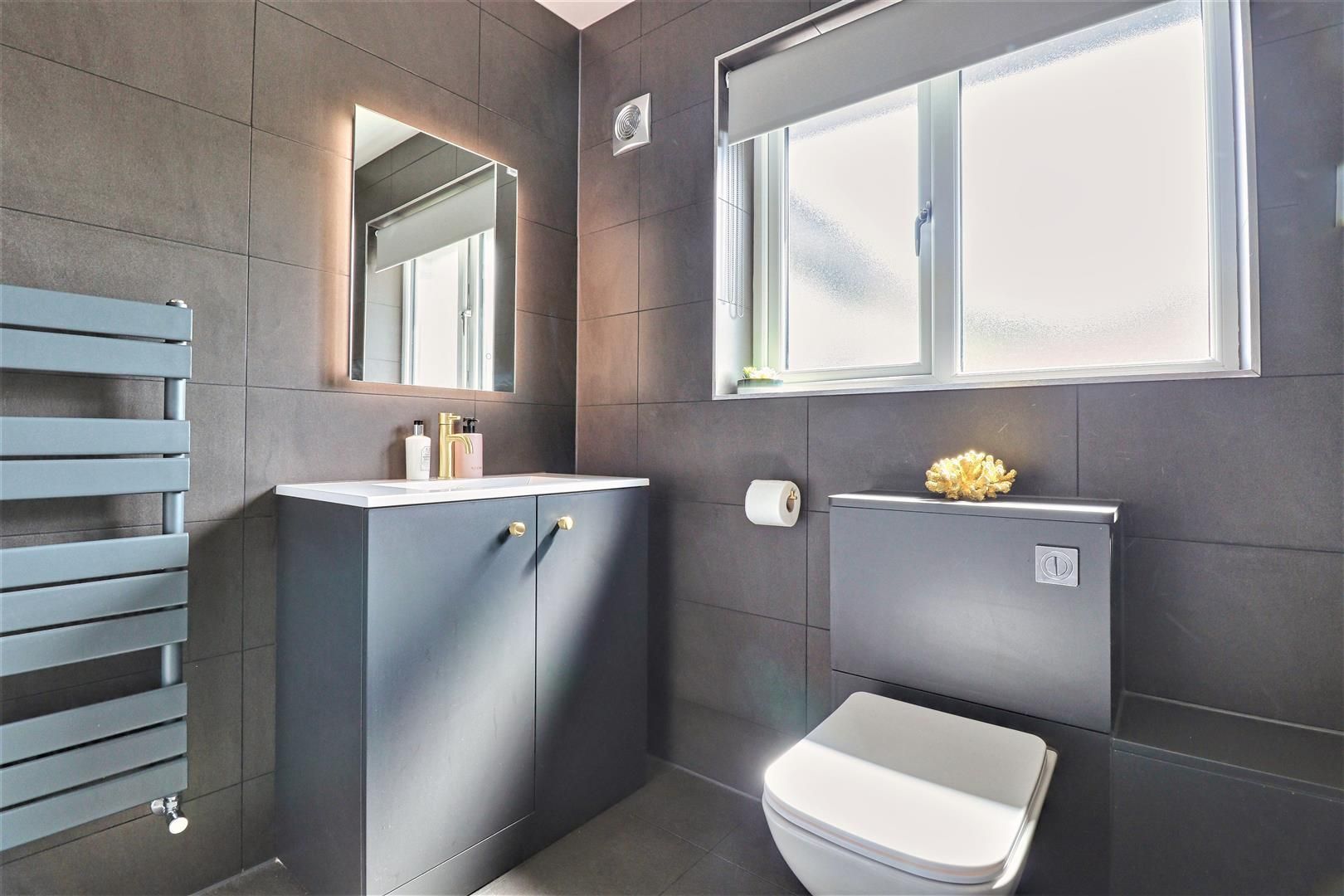 Modern bathroom with grey tiles, vanity, and toilet. A radiator and window are also visible.