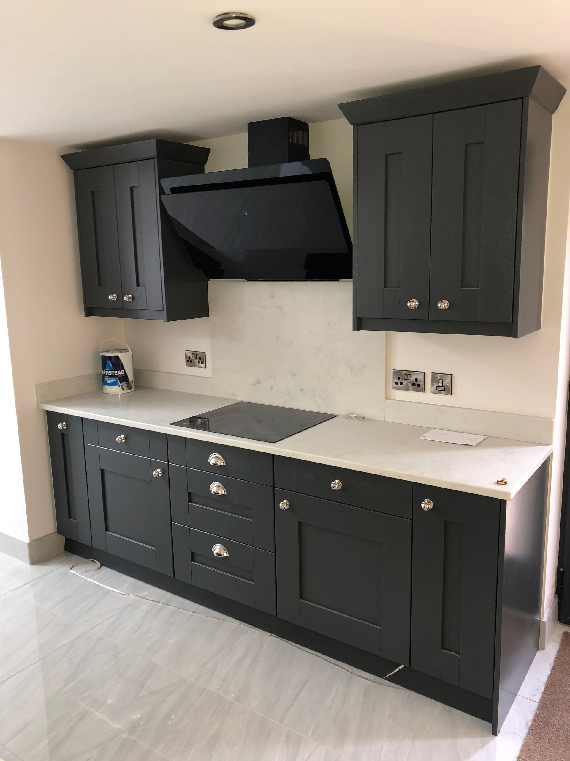 Dark gray kitchen cabinets, cooktop, and range hood with a white countertop.