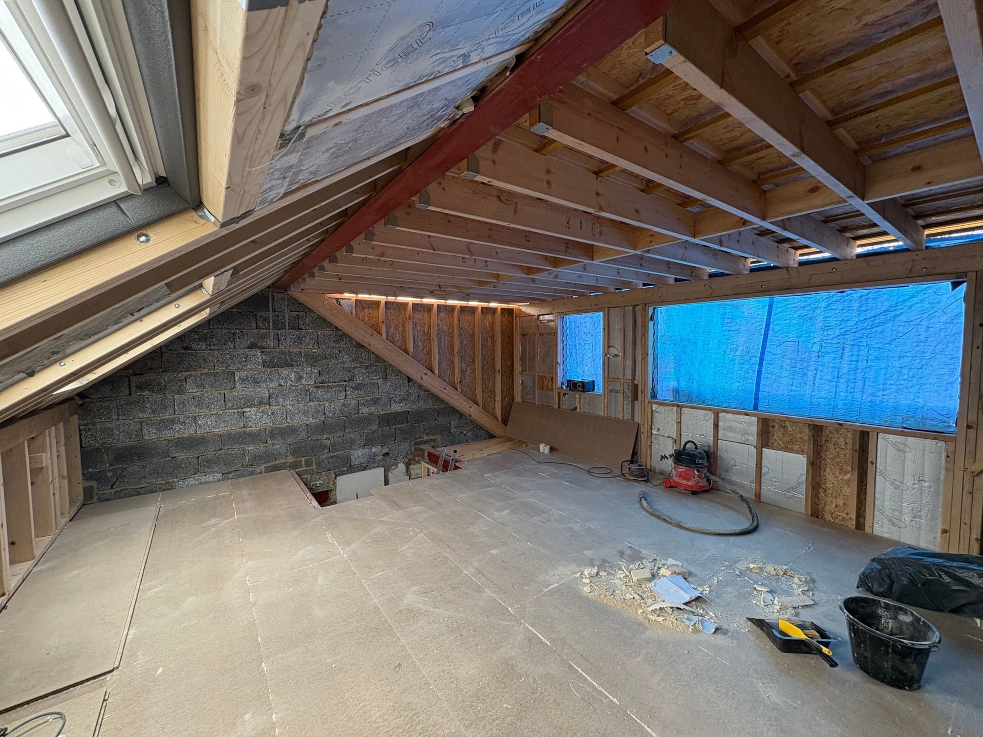 Interior view of an unfinished attic renovation with exposed wood framing, skylight, and stone wall.
