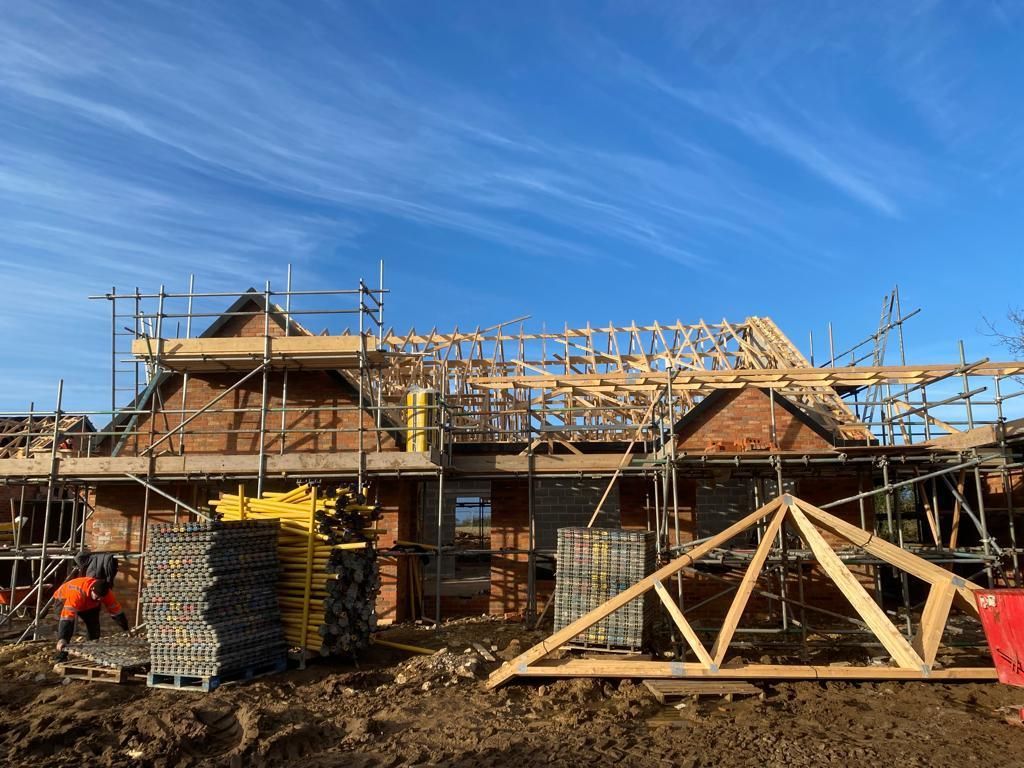 Construction site with brick building, scaffolding, and roof trusses against a blue sky.