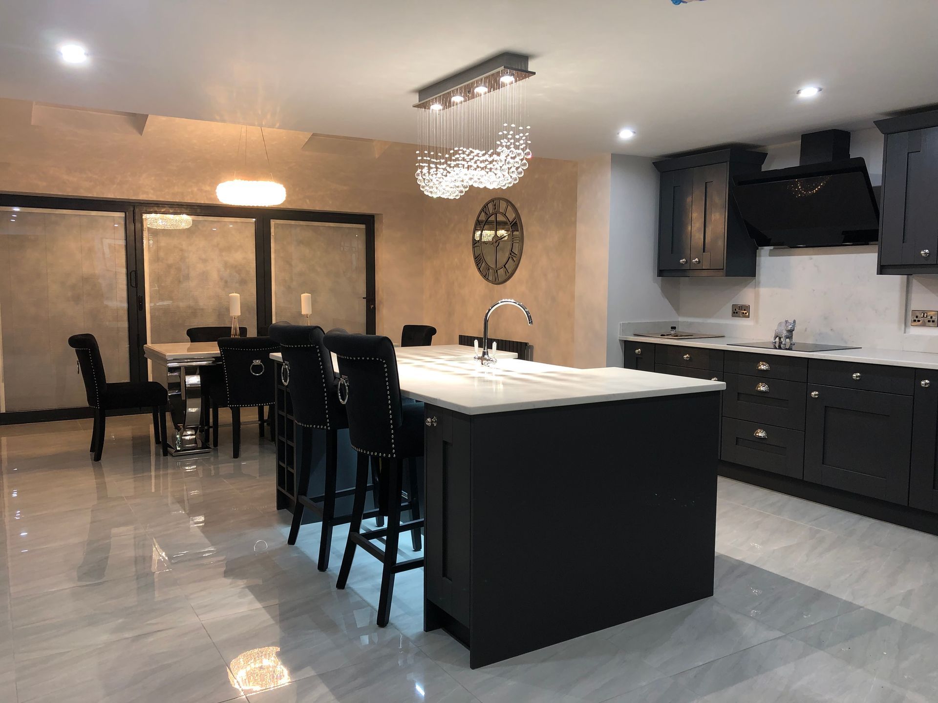 Modern kitchen with dark cabinets, island with bar stools, dining area, and chandelier lighting.