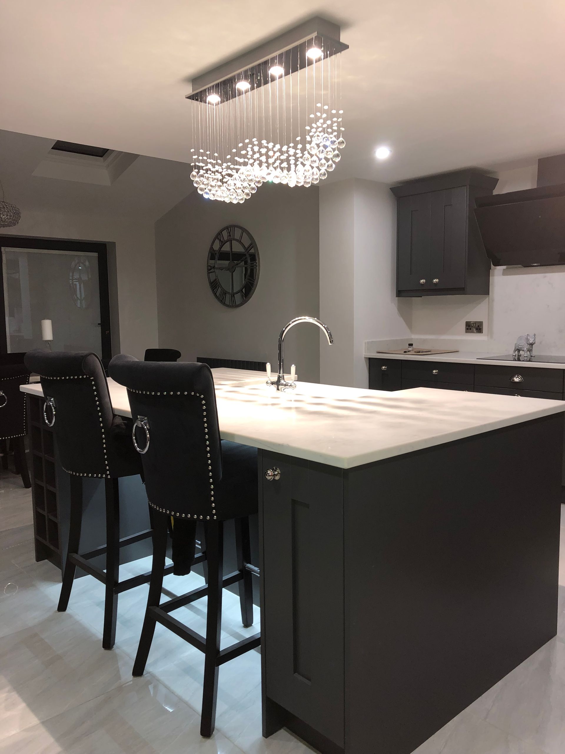 Modern kitchen with dark cabinets, white countertops, island with bar stools, and crystal chandelier.