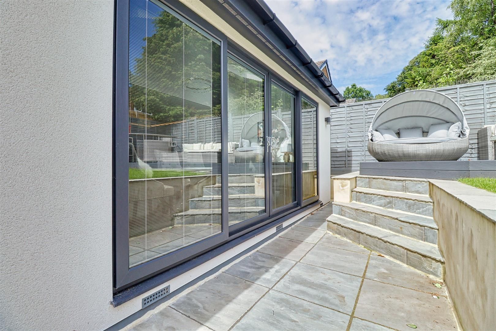 Sliding glass doors open to a patio with steps, a seating pod, and a manicured backyard.