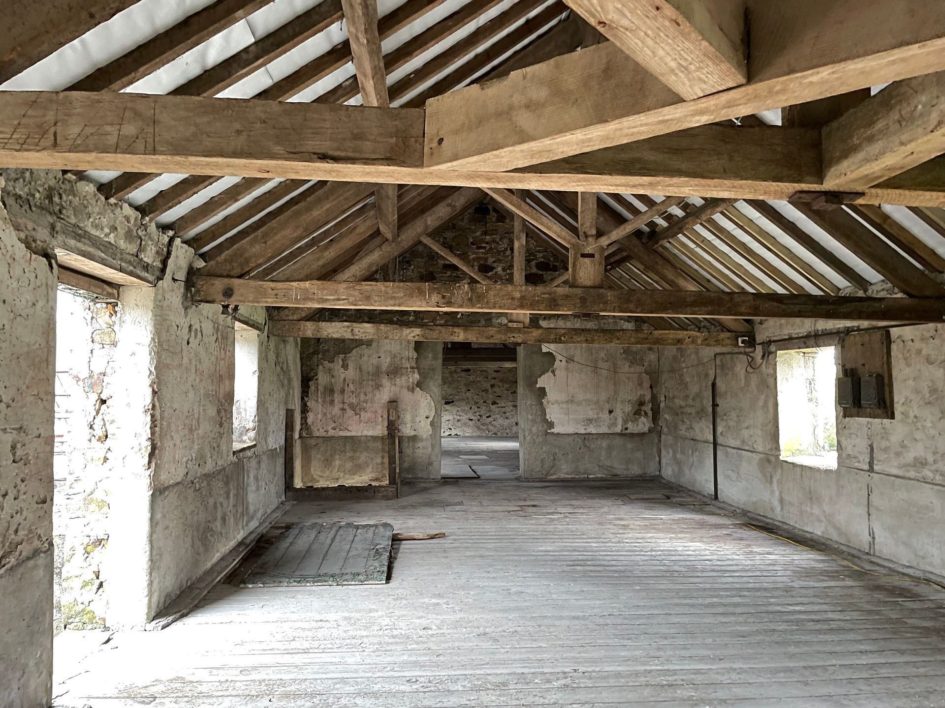 Interior of an old, weathered building with exposed wooden beams and distressed walls, natural light through windows.