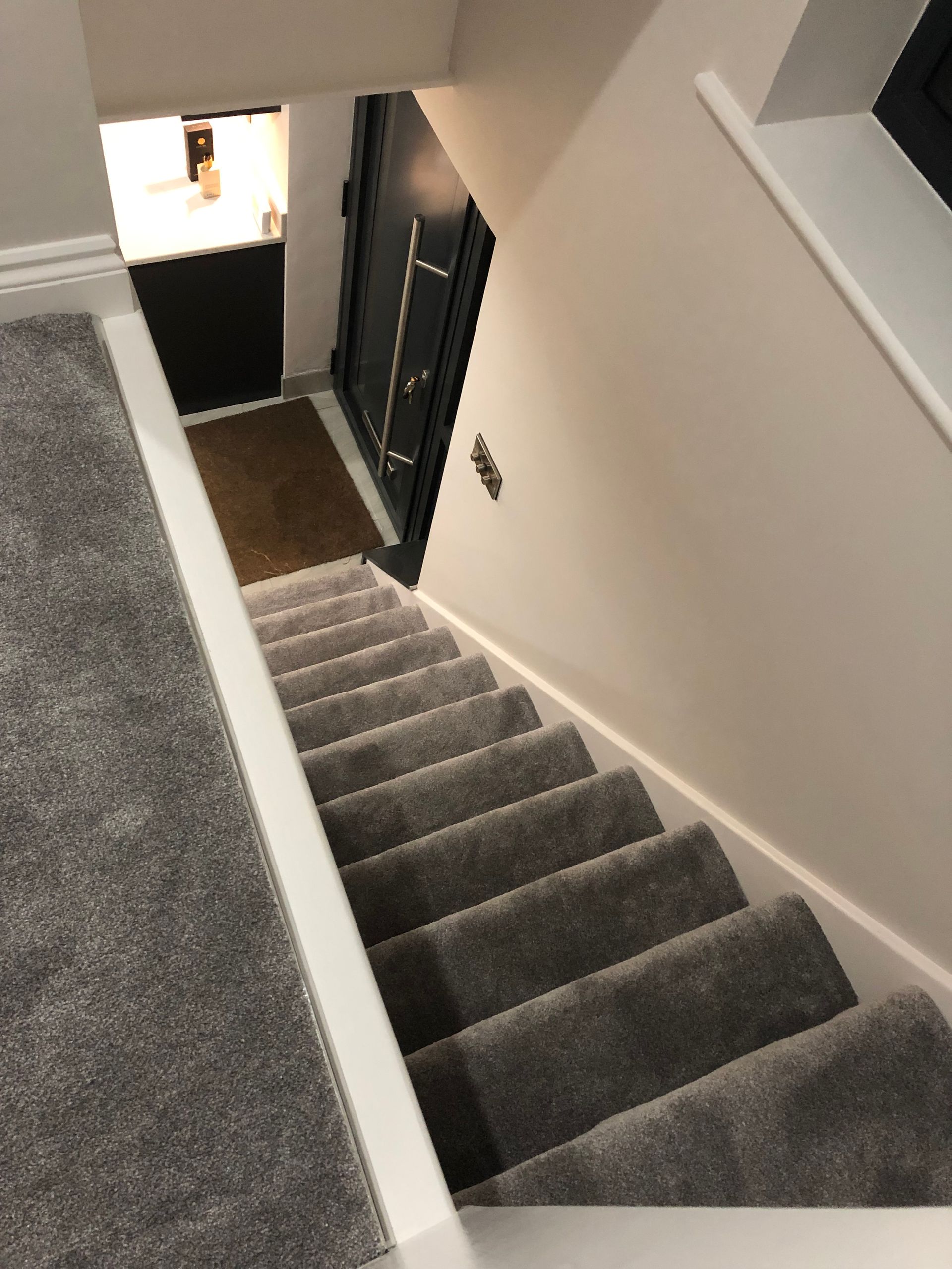 Staircase with gray carpet leading downwards, white walls and trim, door at the bottom.