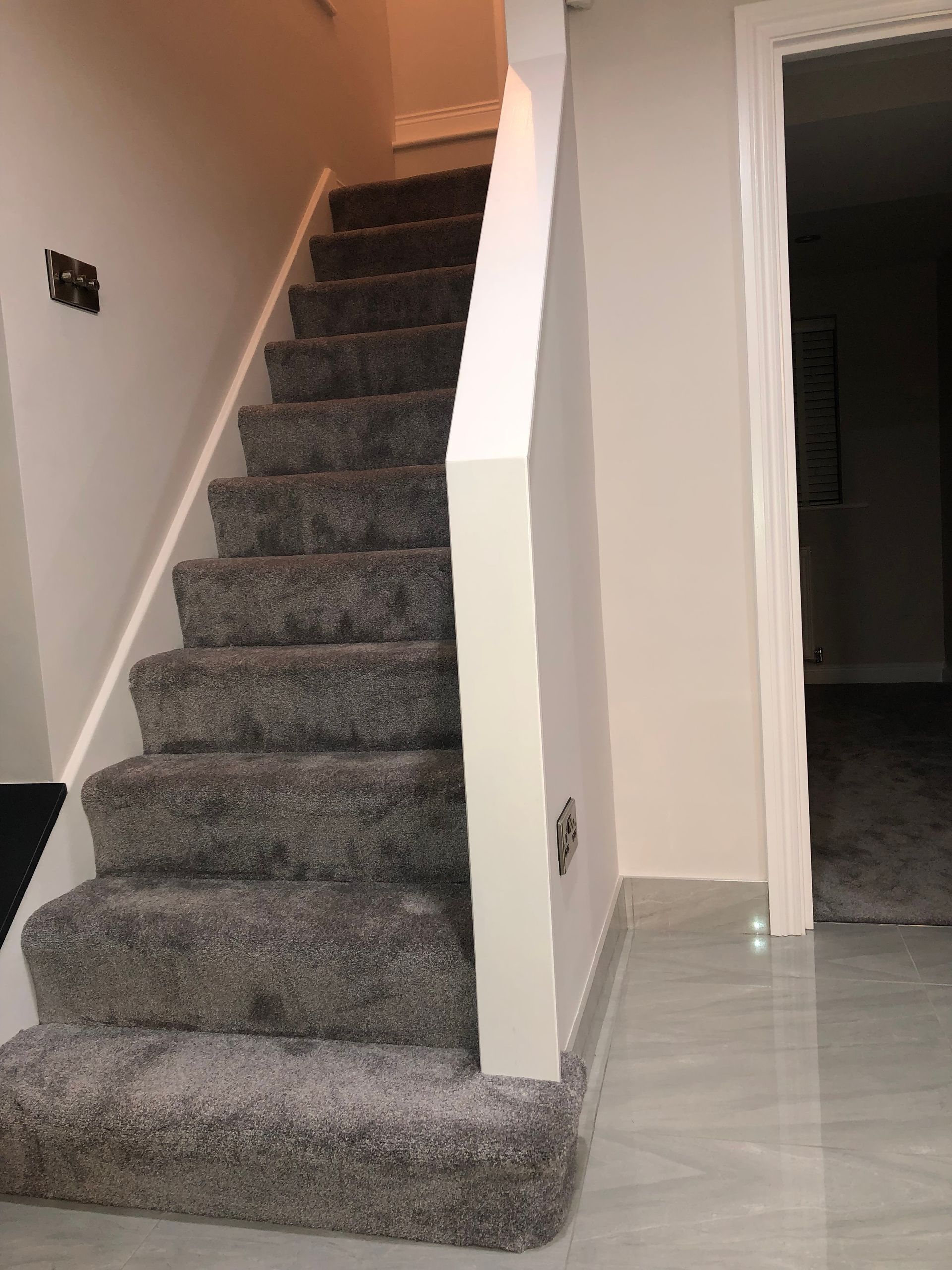 Gray carpeted staircase with white trim, leading upward. Gray flooring and a doorway visible.