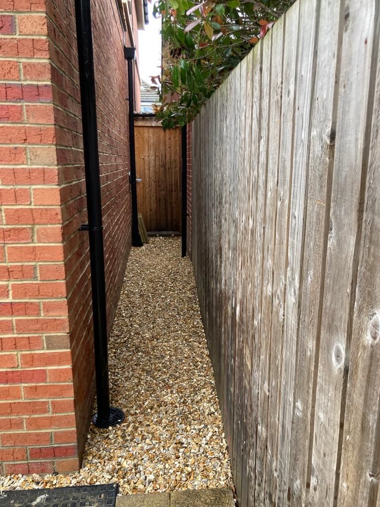 Narrow gravel pathway between a brick wall and wooden fence, leading to a gate.