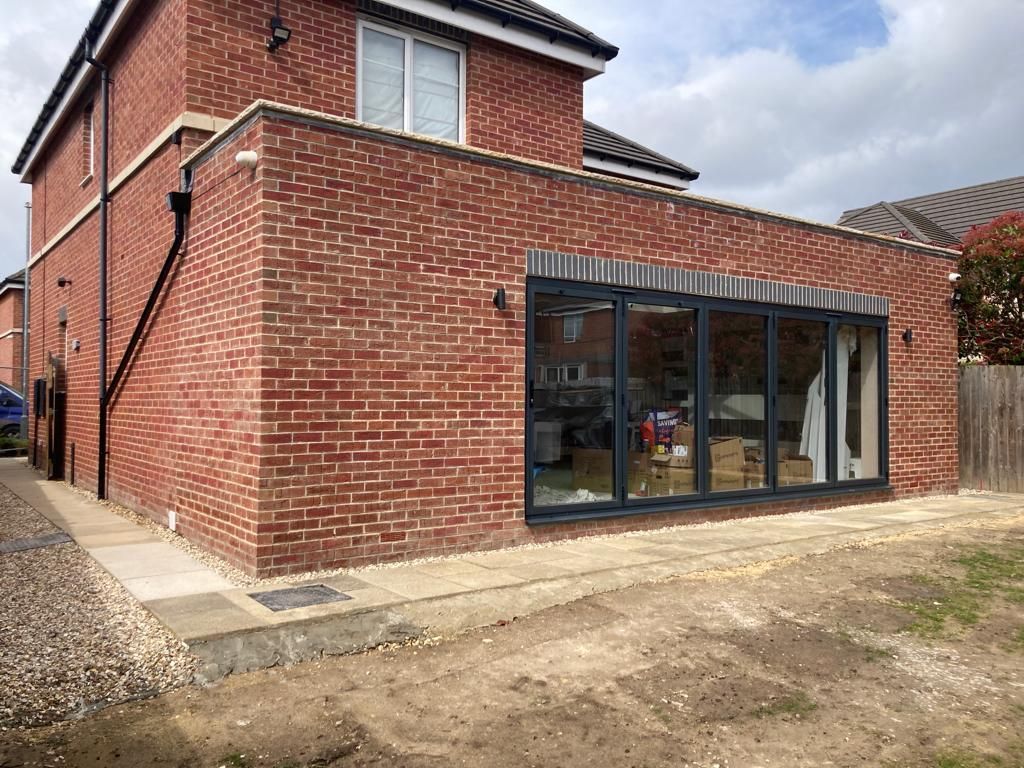 Red brick house extension with large glass doors.
