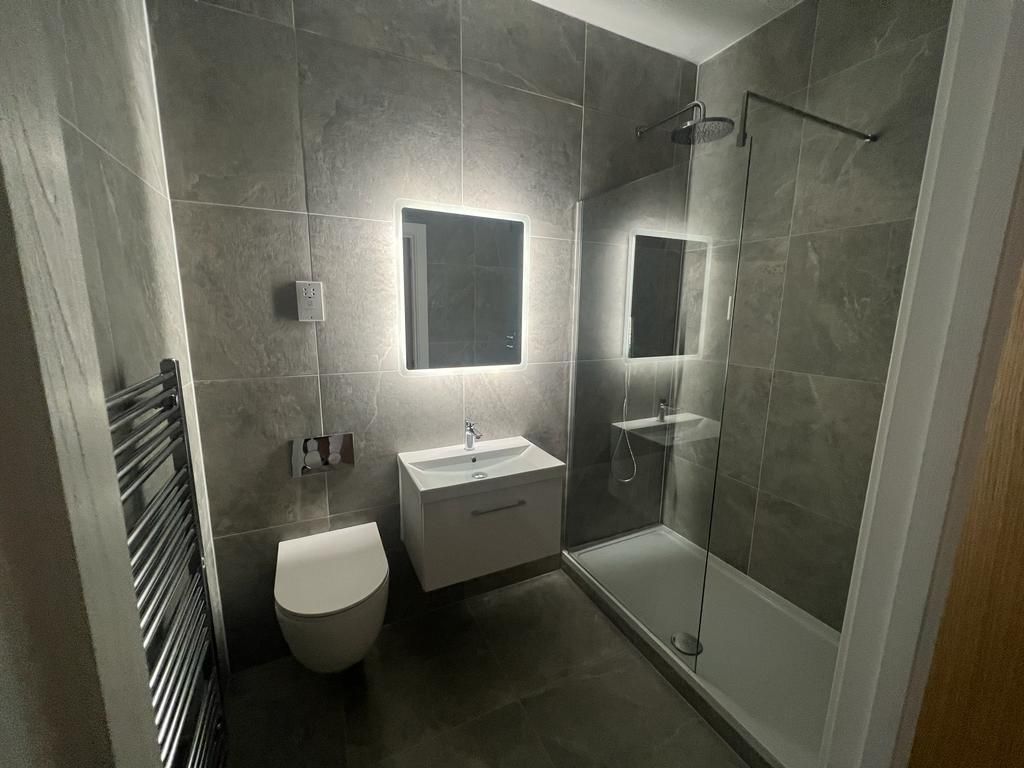 Modern gray tiled bathroom with illuminated mirror, shower, toilet, and heated towel rack.
