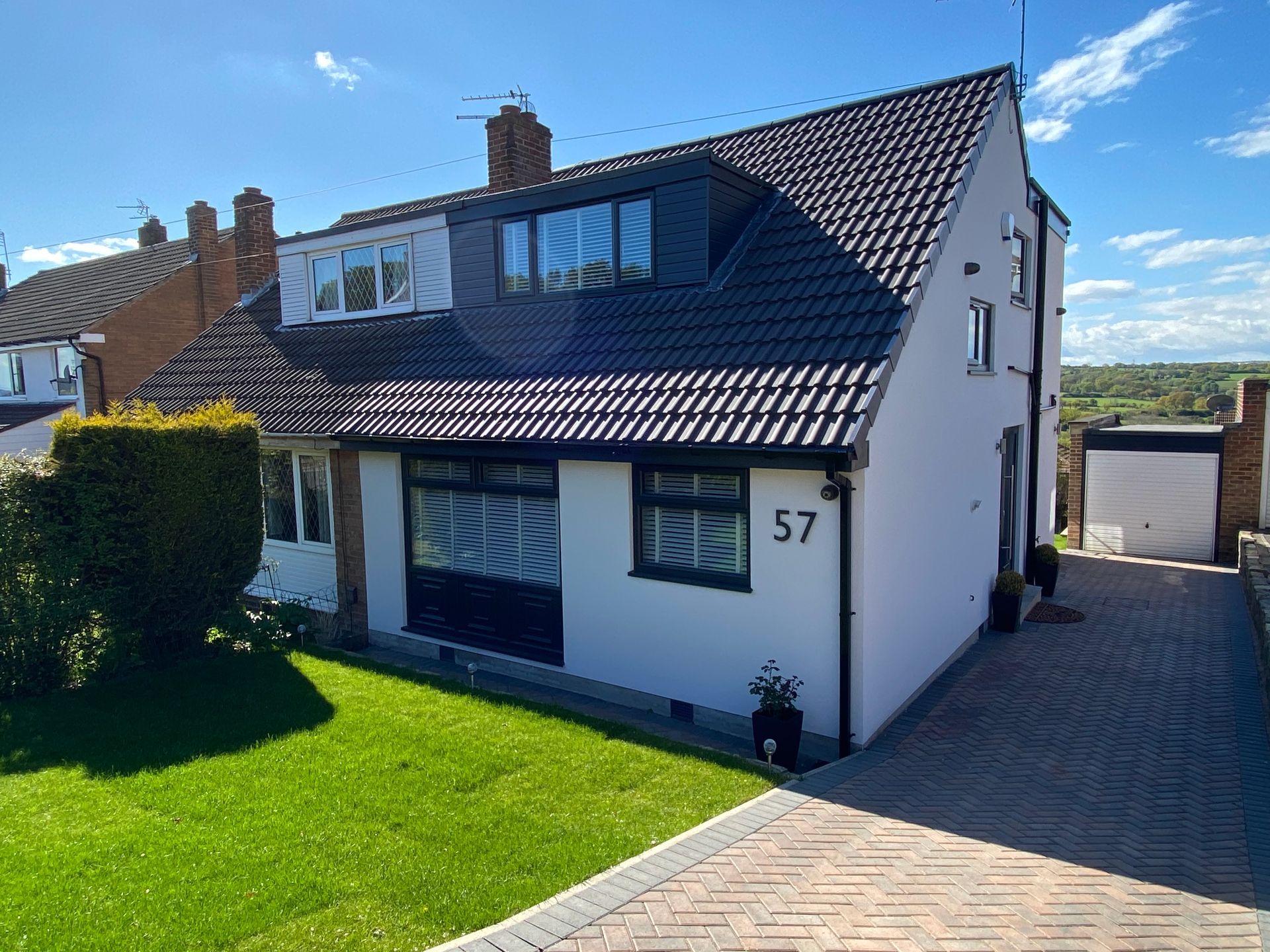 White house with black roof and dormer, green lawn, and a paved driveway. Number