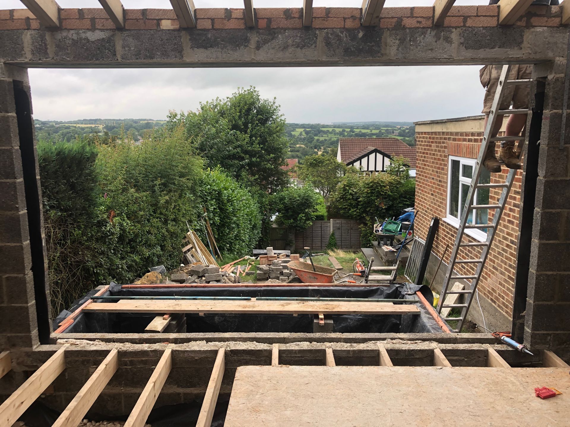 Construction site: unfinished room with view of green trees, homes, and cloudy sky.