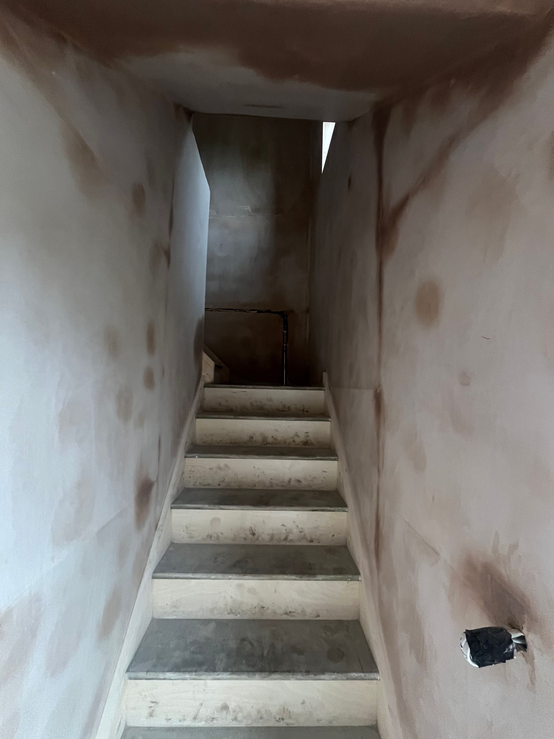 Staircase with concrete steps, unfinished walls with brown marks. The opening at the top is visible.