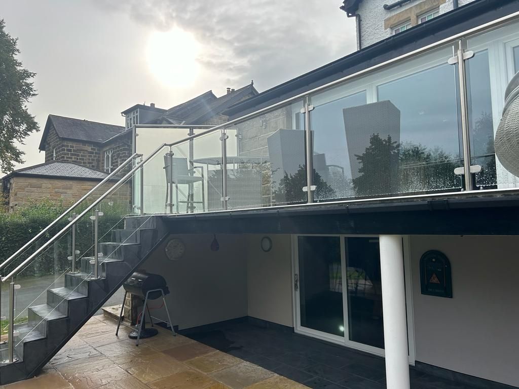 A deck with glass railings and stairs, overlooking a patio; the sky is overcast.