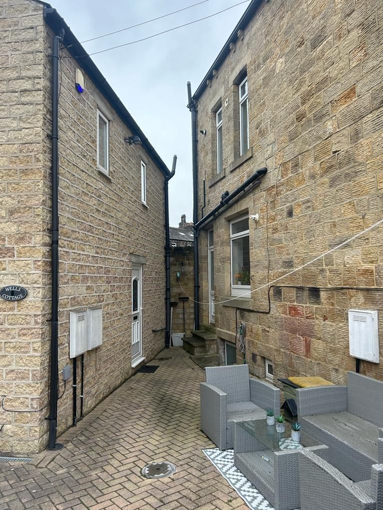 Narrow alleyway between two stone buildings, with outdoor seating and a cloudy sky.