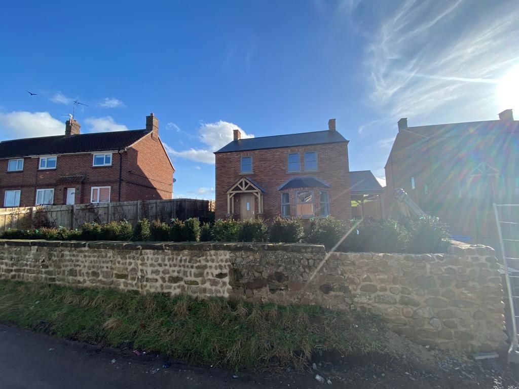 Brick houses on a sunny day, one with a porch, behind a stone wall and greenery.