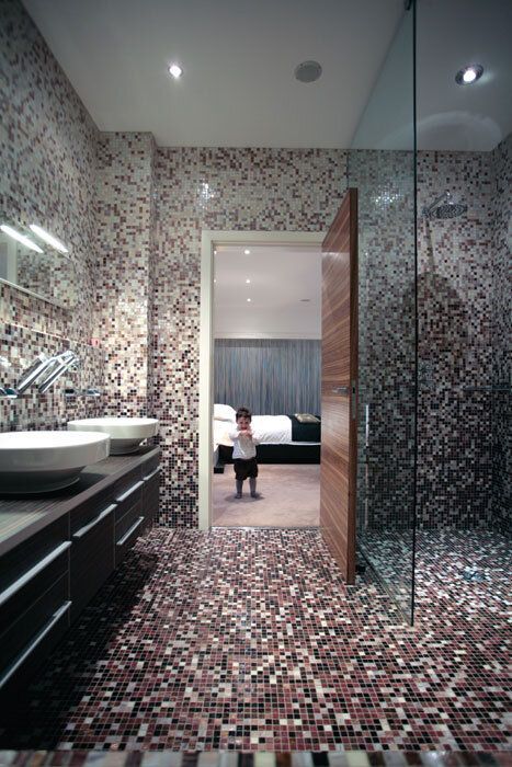 Mosaic-tiled bathroom with a child standing in a doorway to a bedroom. Modern design, neutral tones.
