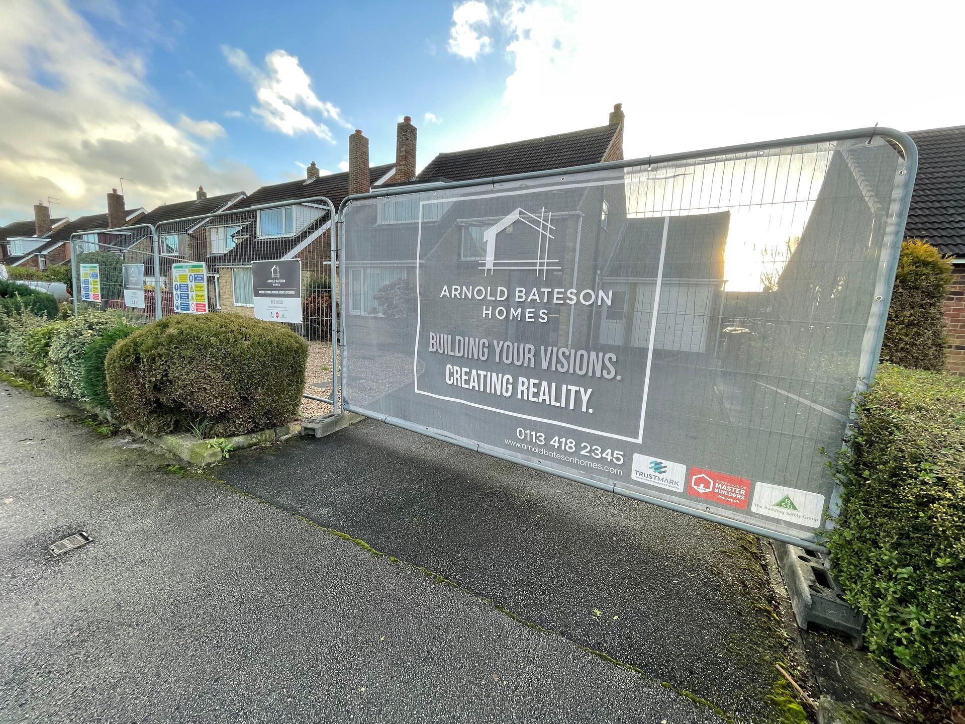 Construction site with fence, sign for Arnold Bateson Homes, houses in background.