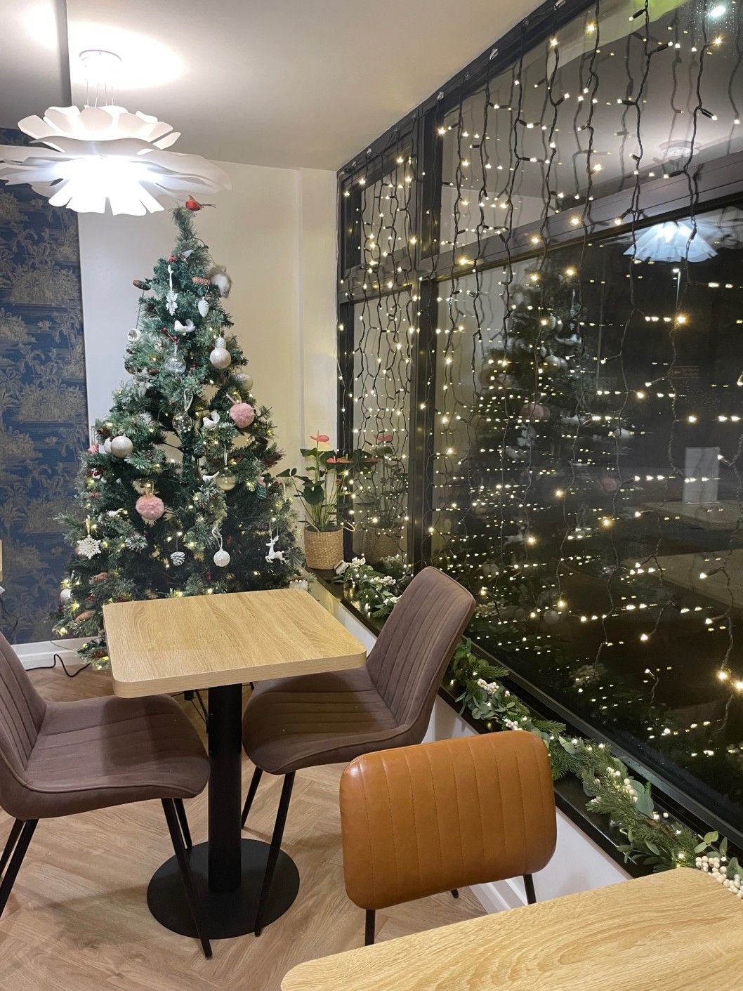 Cozy cafe corner with Christmas tree, table, chairs, and twinkling lights against a city view.