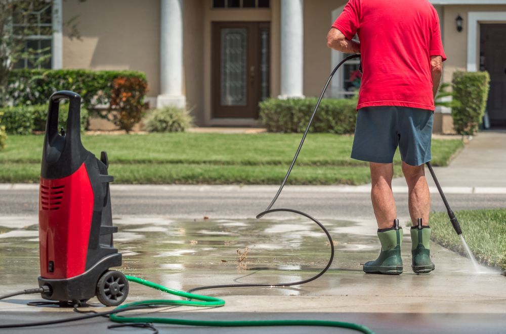 Person Pressure-washing a Driveway Beside a Red Washer — Ausmade Services Pty Ltd in Chapel Hill, QLD