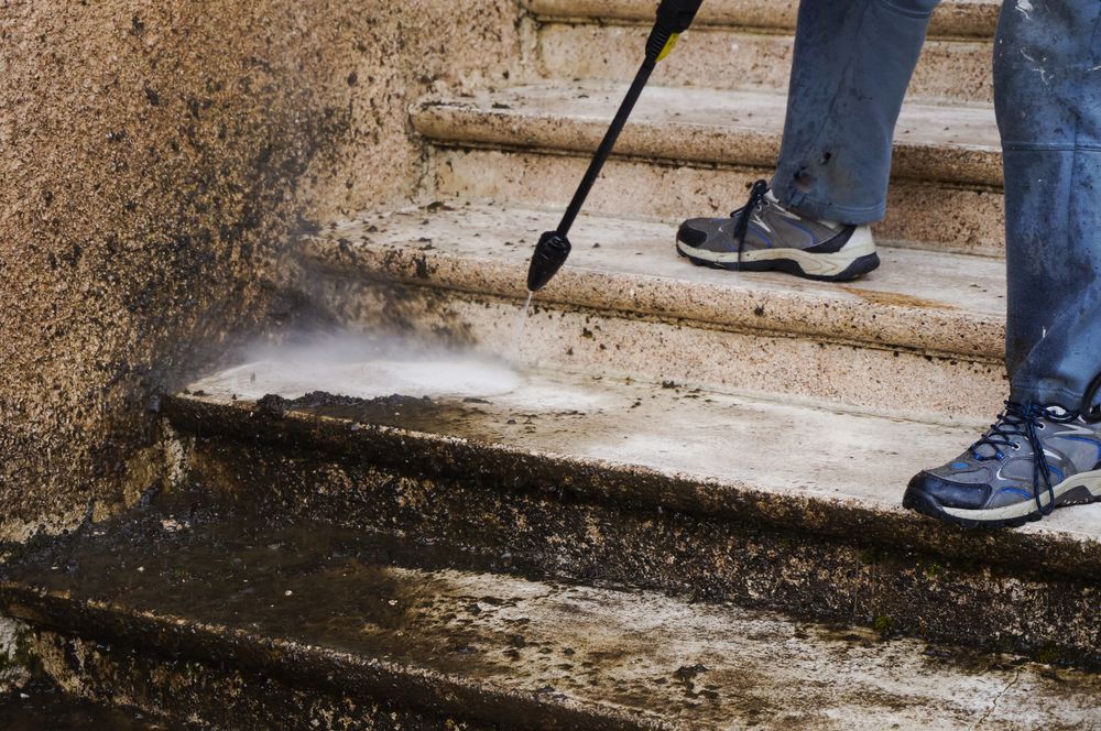 A Person is Cleaning a Set of Stairs With a High Pressure Washer — Ausmade Services Pty Ltd in Brisbane, QLD