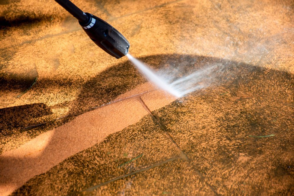 A Person is Using a High Pressure Washer to Clean a Concrete Surface — Ausmade Services Pty Ltd in Brisbane, QLD