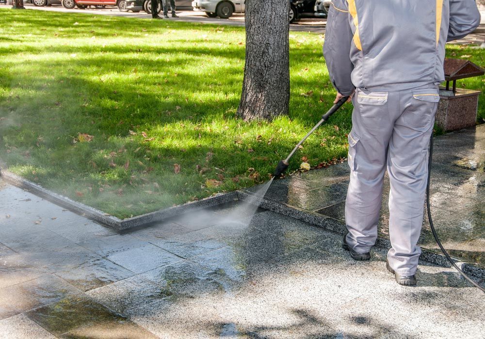 A Man is Using a High Pressure Washer to Clean a Sidewalk — Ausmade Services Pty Ltd in Brisbane, QLD