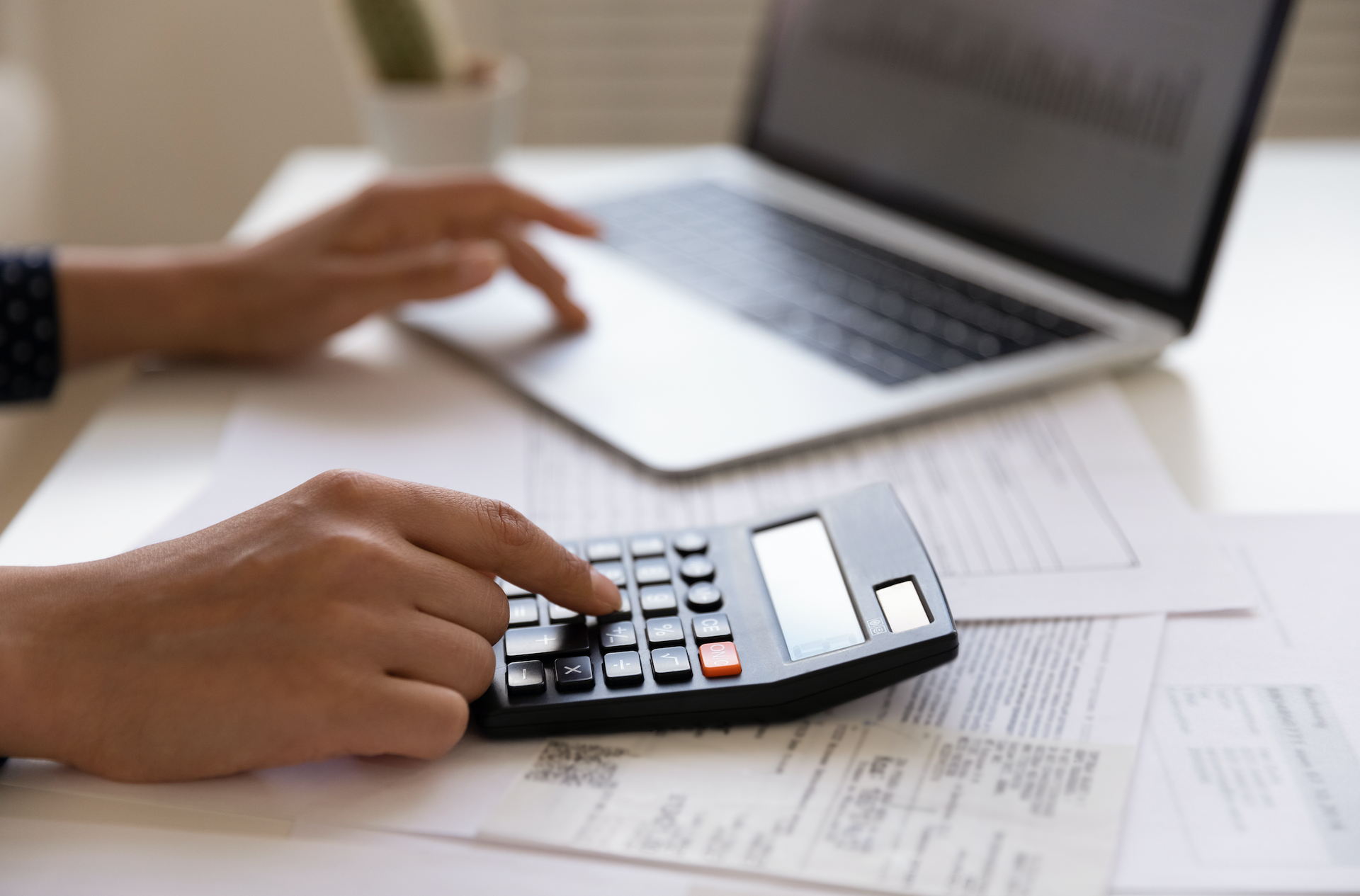 A person is using a calculator in front of a laptop computer.