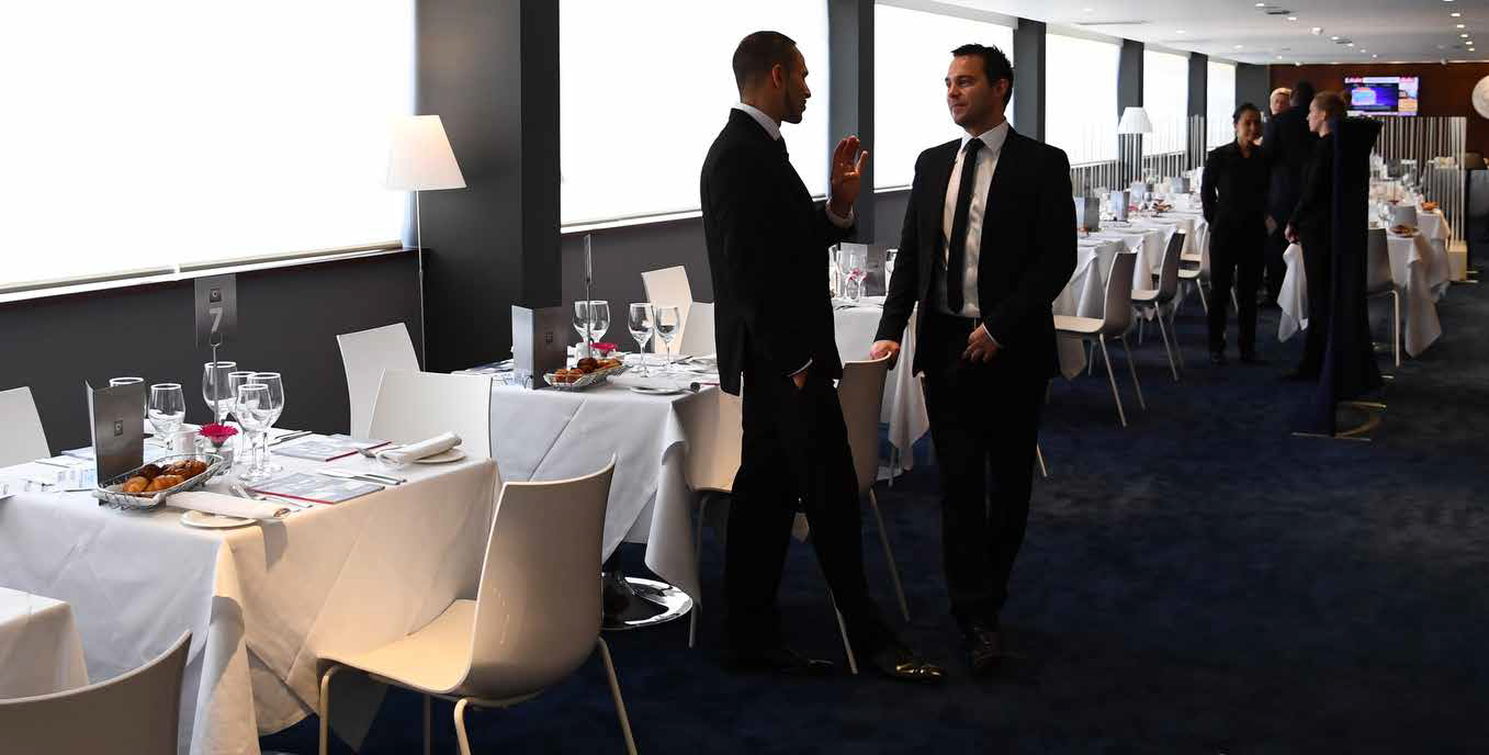 Conference room reception with two men talking beside set dining tables and other guests in the background