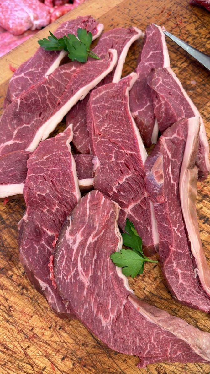 Fette di manzo crudo marmorizzato su un tagliere di legno, guarnite con prezzemolo.
